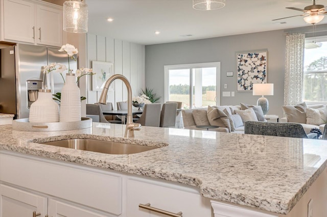 kitchen featuring light stone counters, ceiling fan, sink, white cabinets, and stainless steel fridge with ice dispenser