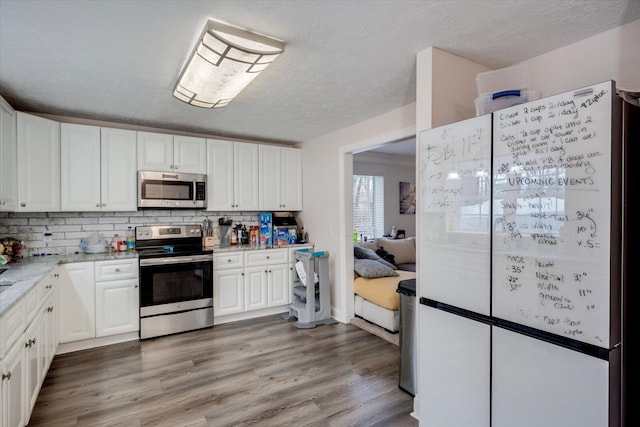 kitchen featuring light stone counters, stainless steel appliances, wood-type flooring, and white cabinets