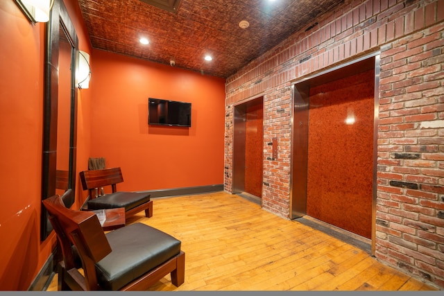 hall with light hardwood / wood-style floors and brick wall