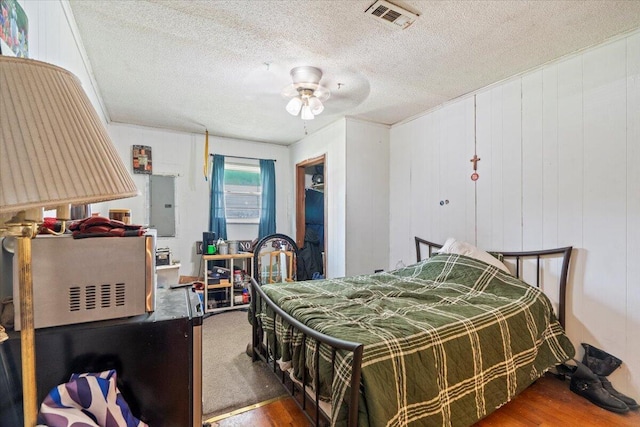 bedroom featuring a textured ceiling, ceiling fan, wood walls, and dark wood-type flooring