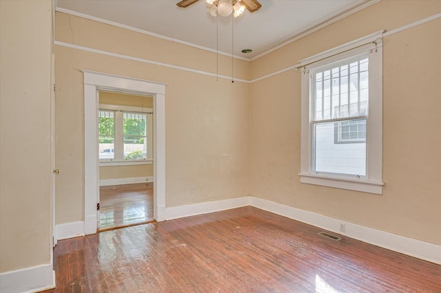 spare room featuring wood-type flooring, ornamental molding, ceiling fan, and a healthy amount of sunlight