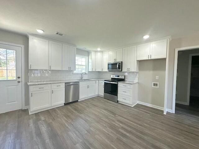 kitchen featuring appliances with stainless steel finishes, tasteful backsplash, sink, hardwood / wood-style flooring, and white cabinets