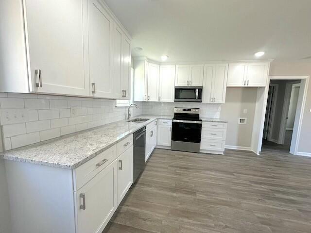 kitchen featuring light stone countertops, appliances with stainless steel finishes, dark wood-type flooring, sink, and white cabinets