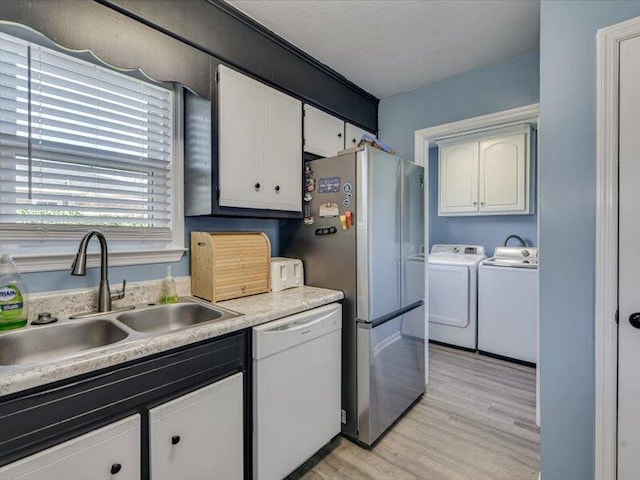 kitchen featuring a sink, white cabinetry, white dishwasher, light wood finished floors, and washing machine and clothes dryer