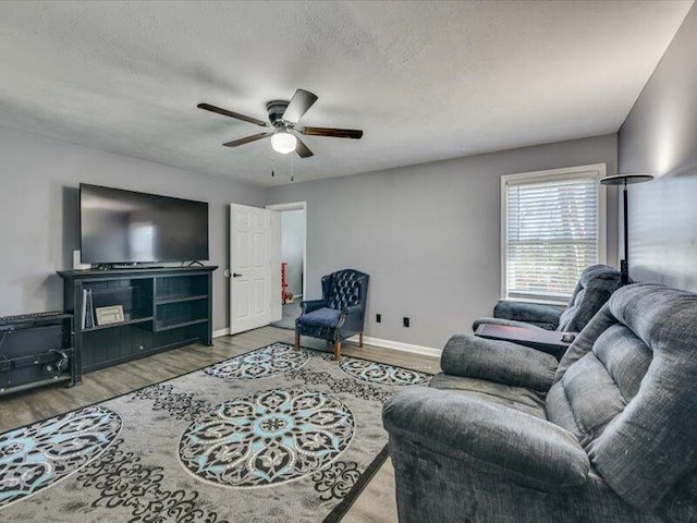 living area with ceiling fan, wood finished floors, baseboards, and a textured ceiling