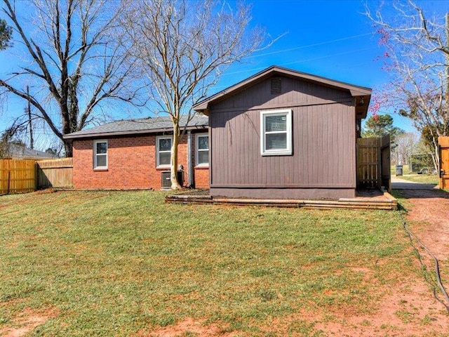 rear view of house featuring brick siding, a lawn, and fence