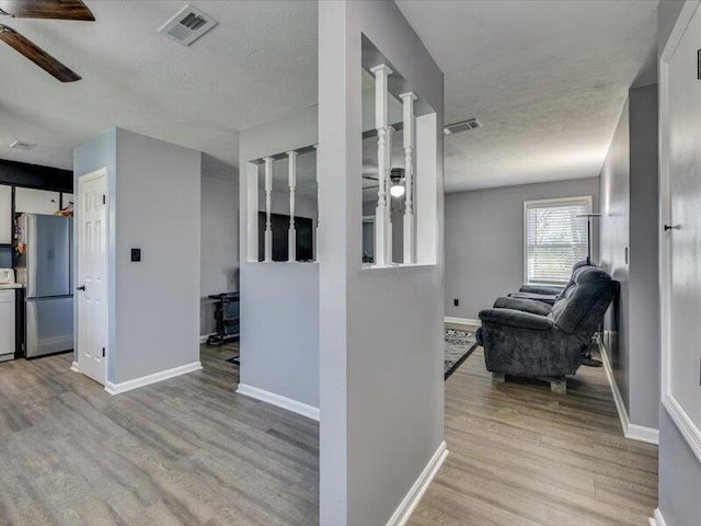 hallway featuring visible vents, baseboards, a textured ceiling, and wood finished floors