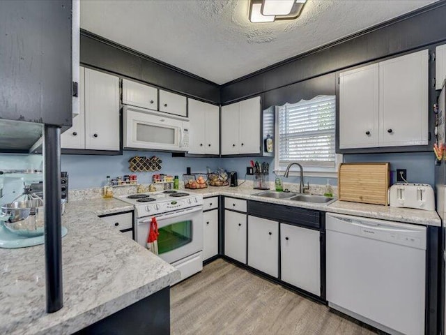 kitchen with white appliances, white cabinetry, light countertops, and a sink