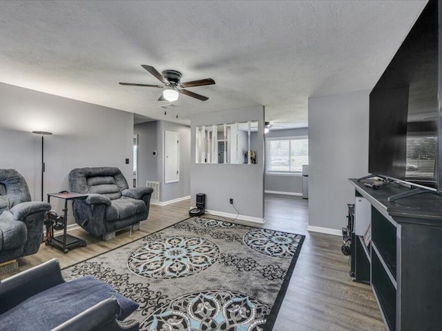 living area with wood finished floors, a ceiling fan, baseboards, and a textured ceiling