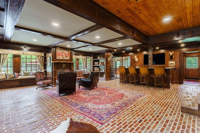 living room with beam ceiling, coffered ceiling, built in features, wood walls, and indoor bar