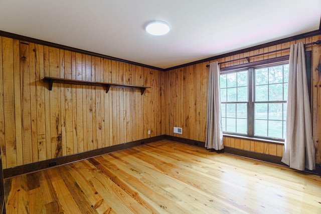 empty room featuring light wood-type flooring, ornamental molding, and wood walls