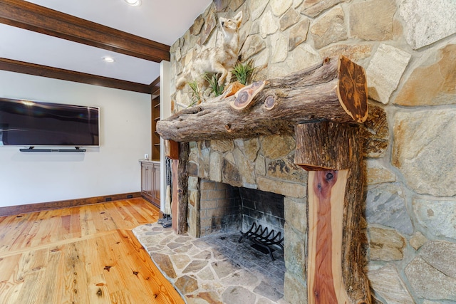 unfurnished living room with beamed ceiling, a stone fireplace, ornamental molding, and hardwood / wood-style flooring