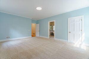 unfurnished bedroom with light colored carpet, ensuite bath, a closet, and crown molding