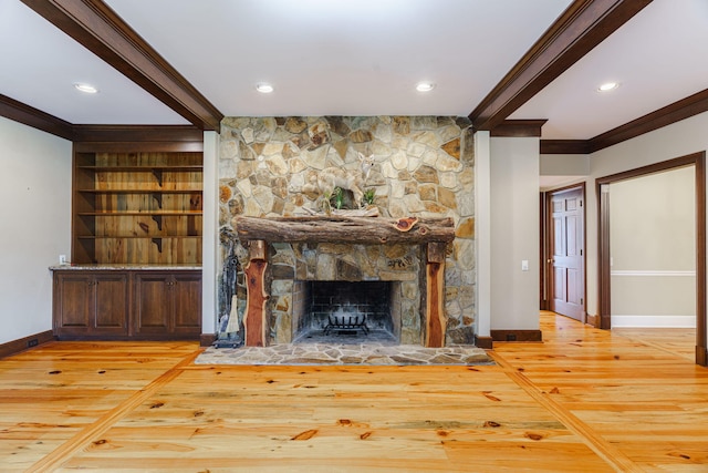 unfurnished living room featuring light hardwood / wood-style floors, built in features, ornamental molding, and a stone fireplace