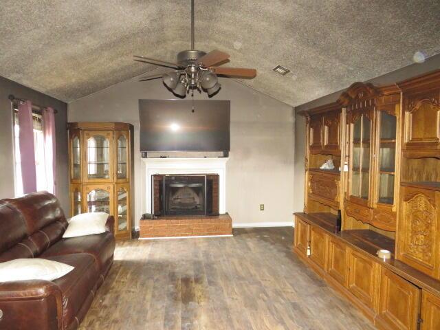 living room with ceiling fan, wood-type flooring, lofted ceiling, and a brick fireplace