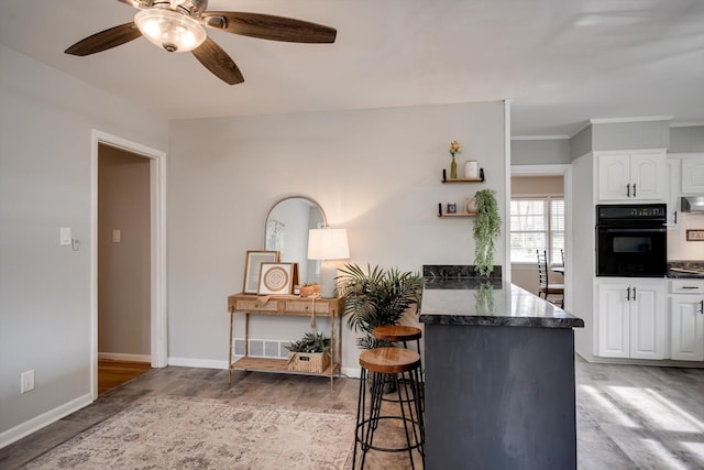 kitchen with oven, a kitchen bar, white cabinets, a ceiling fan, and a peninsula