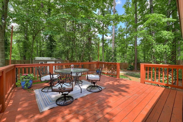 wooden deck featuring outdoor dining area, a storage unit, a fenced backyard, an outdoor structure, and view of wooded area