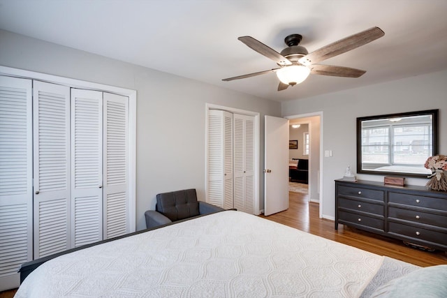 bedroom with multiple closets, wood finished floors, ceiling fan, and baseboards