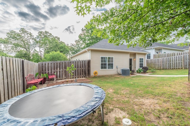 back of property with a lawn, a fenced backyard, a trampoline, and central AC unit