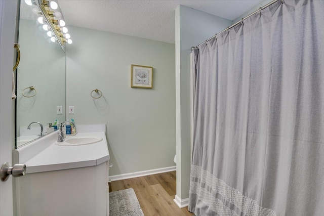 full bath with toilet, a textured ceiling, vanity, wood finished floors, and baseboards