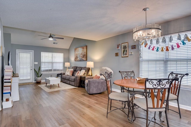 dining area featuring a textured ceiling, ceiling fan with notable chandelier, baseboards, vaulted ceiling, and light wood finished floors