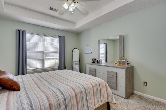 bedroom with baseboards, visible vents, light colored carpet, ceiling fan, and a tray ceiling