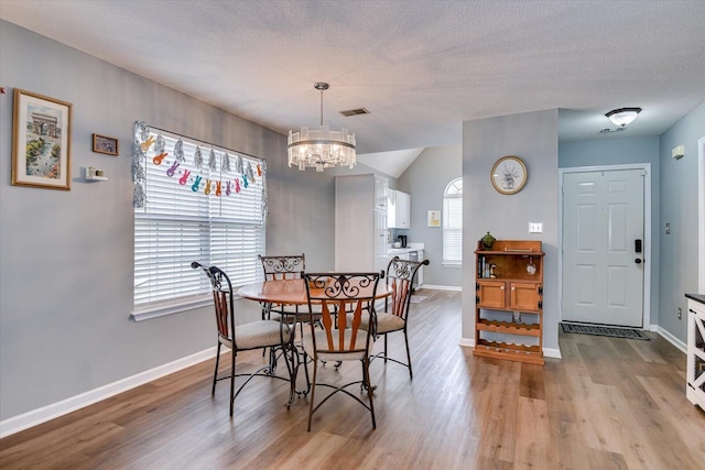 dining area featuring a chandelier, a textured ceiling, baseboards, and wood finished floors