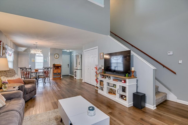 living area with stairs, an inviting chandelier, wood finished floors, and baseboards