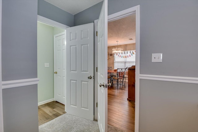 corridor with baseboards, a textured ceiling, an inviting chandelier, and wood finished floors