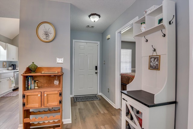 mudroom with light wood-style floors, baseboards, visible vents, and a textured ceiling