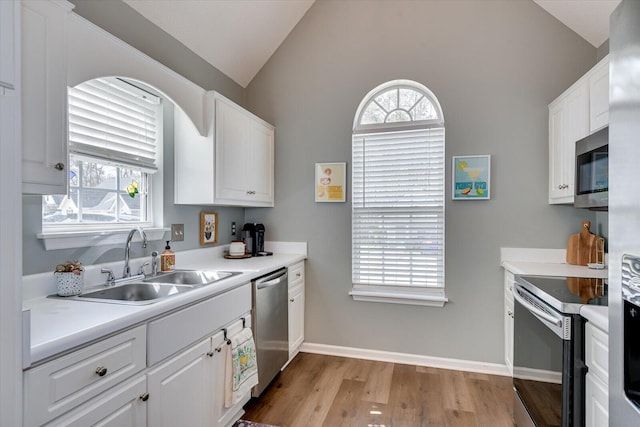 kitchen featuring light wood finished floors, white cabinets, appliances with stainless steel finishes, vaulted ceiling, and a sink