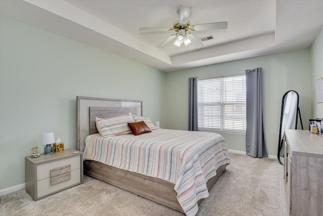 bedroom featuring light carpet, baseboards, visible vents, and a raised ceiling