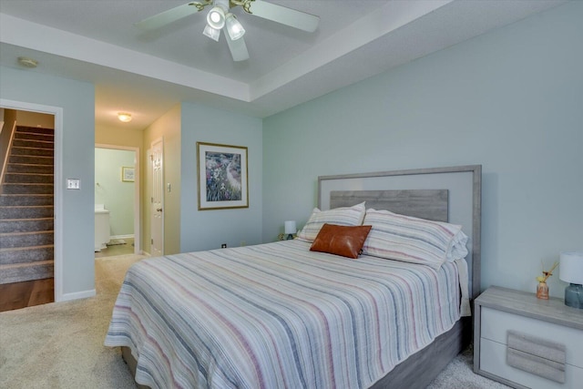 bedroom with baseboards, a raised ceiling, a ceiling fan, ensuite bath, and carpet