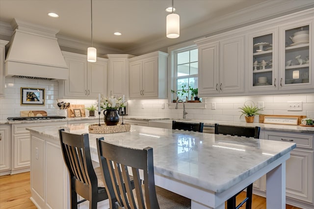 710 Nuttall St, Evans, GA 30809 - kitchen featuring custom range hood, a breakfast bar, stainless steel gas cooktop, glass insert cabinets, and light stone counters