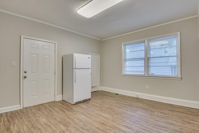 unfurnished bedroom featuring light hardwood / wood-style flooring, white fridge, a textured ceiling, and ornamental molding