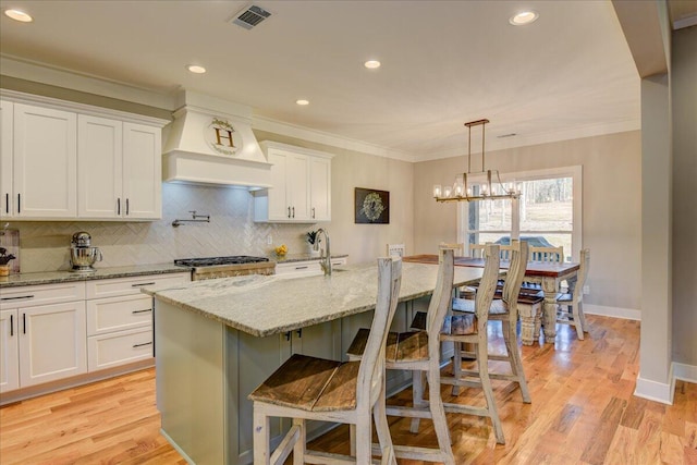 kitchen featuring light stone countertops, a kitchen breakfast bar, white cabinets, light wood-type flooring, and an island with sink