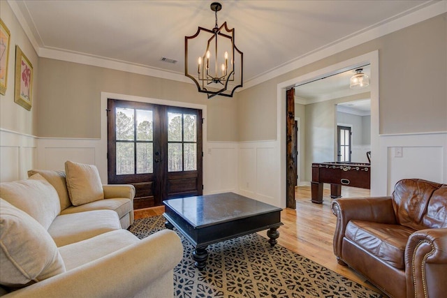 living room with ornamental molding, french doors, light hardwood / wood-style flooring, and an inviting chandelier