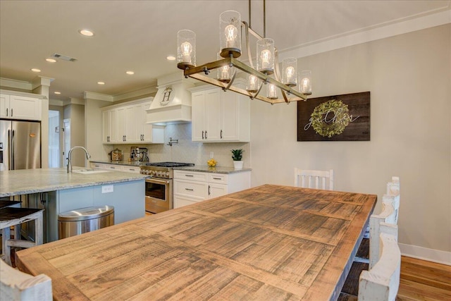 kitchen featuring pendant lighting, premium range hood, white cabinetry, an island with sink, and high end appliances