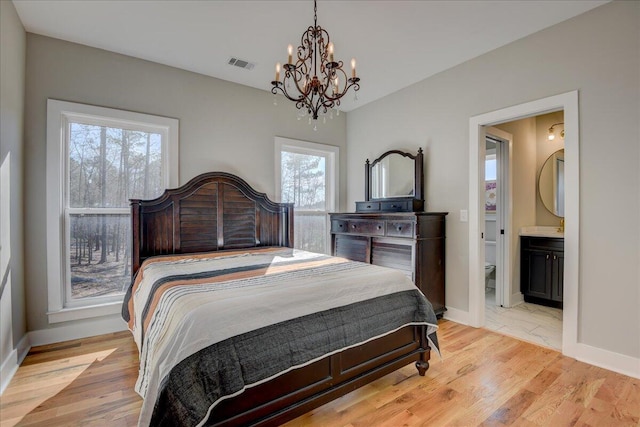 bedroom with multiple windows, ensuite bathroom, a notable chandelier, and light wood-type flooring