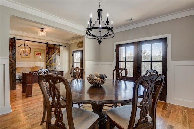 dining area featuring a notable chandelier, light hardwood / wood-style flooring, a barn door, and crown molding