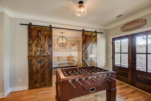 playroom featuring light wood-type flooring, a barn door, and crown molding