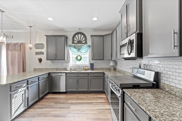 kitchen with sink, kitchen peninsula, pendant lighting, gray cabinets, and appliances with stainless steel finishes