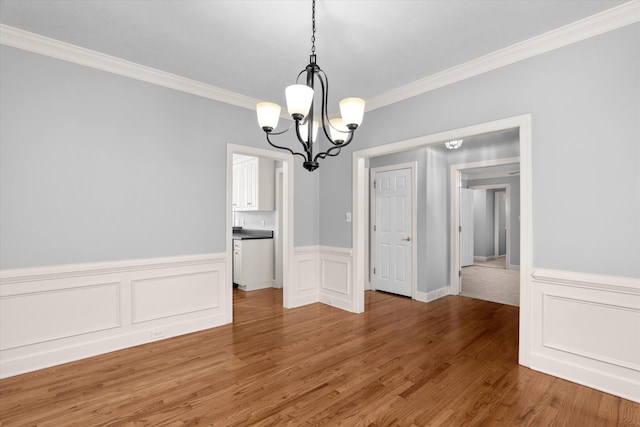 unfurnished dining area featuring an inviting chandelier, crown molding, and wood-type flooring