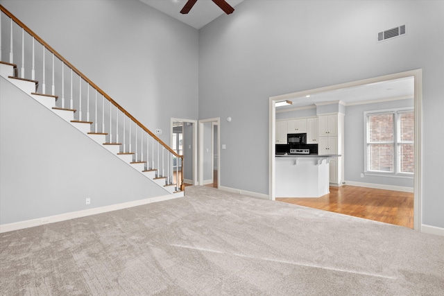 unfurnished living room with a high ceiling, light carpet, and ceiling fan