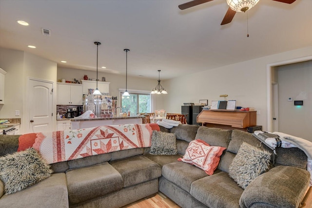 living room with ceiling fan with notable chandelier, light hardwood / wood-style floors, and sink