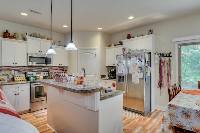 kitchen with a center island with sink, hanging light fixtures, light hardwood / wood-style flooring, white cabinetry, and stainless steel appliances