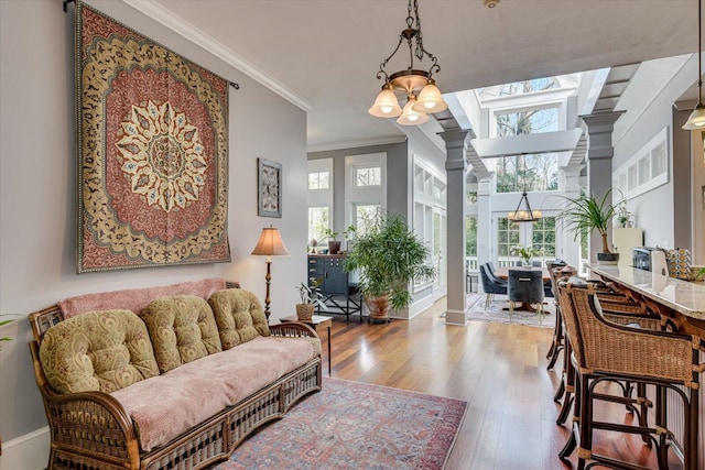 living area with ornate columns, an inviting chandelier, ornamental molding, wood finished floors, and baseboards