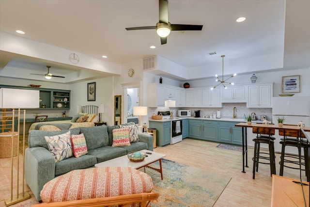 living room with recessed lighting, a raised ceiling, visible vents, light wood-style flooring, and ceiling fan with notable chandelier