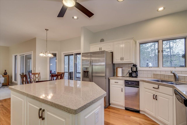 kitchen with stainless steel appliances, a kitchen island, sink, pendant lighting, and white cabinetry