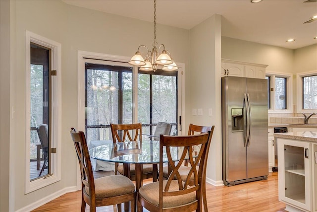 dining space with sink, light hardwood / wood-style floors, and a notable chandelier